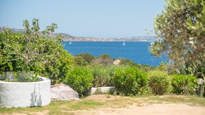 A coastal landscape with a clear view of the sea, greenery, and a white structure in the foreground.