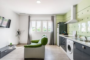 A modern kitchen with a built-in washing machine, a flat-screen TV, and a dining area with a sofa.