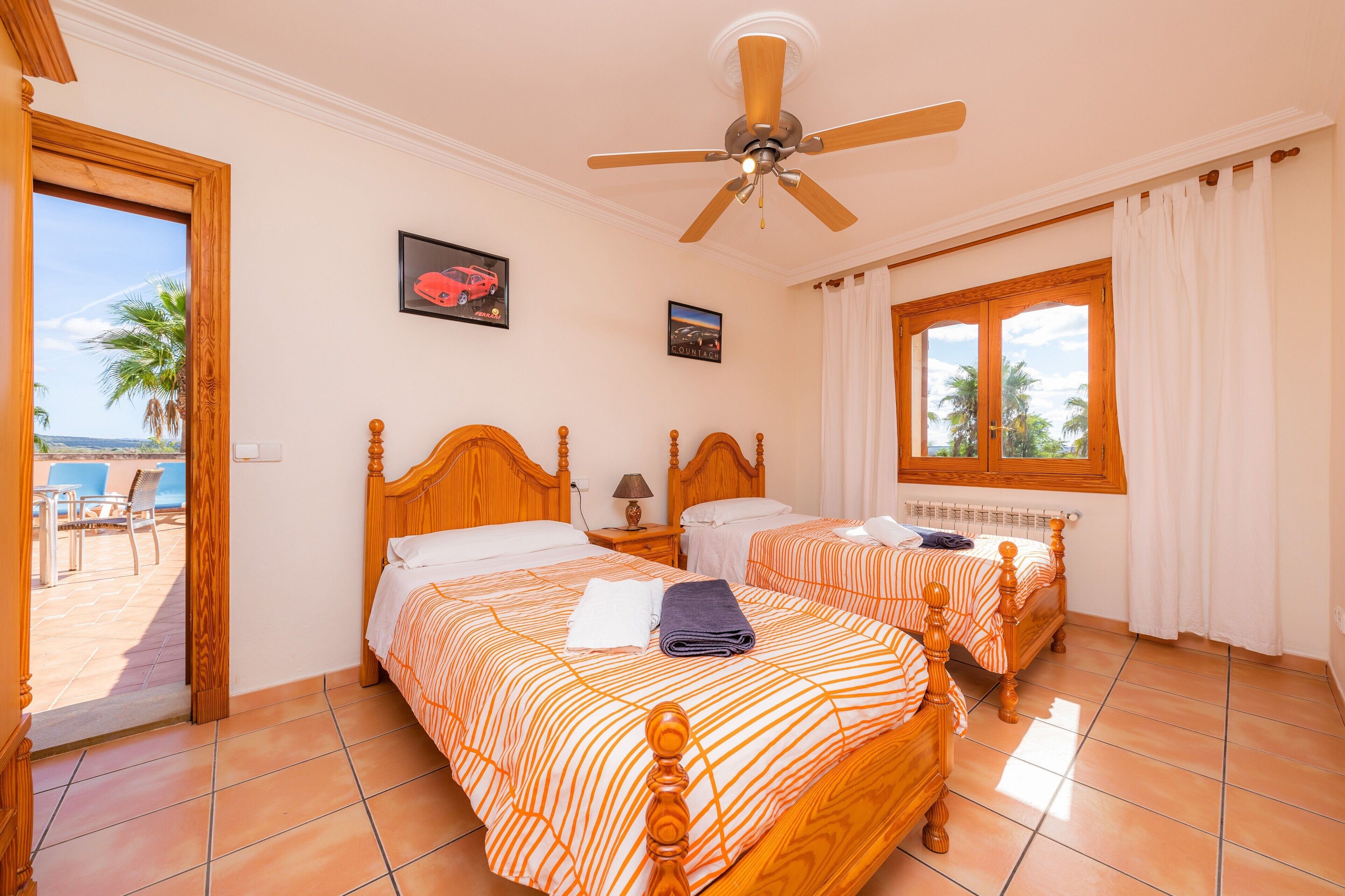 Habitación de hotel con dos camas, ventilador de techo, ventana con cortinas y vistas a palmeras.