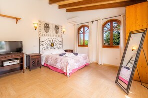 Ein Schlafzimmer mit Bett, Fernseher, Nachttisch, Kleiderschrank und einem Fenster mit Vorhängen.