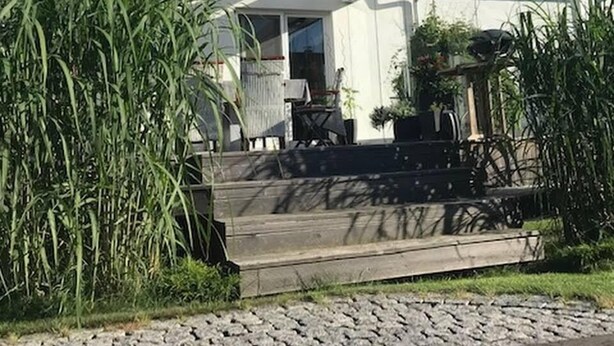 Un espace extérieur abrité, doté d’une terrasse en bois, d’un escalier menant à une porte et de plantes en pot.