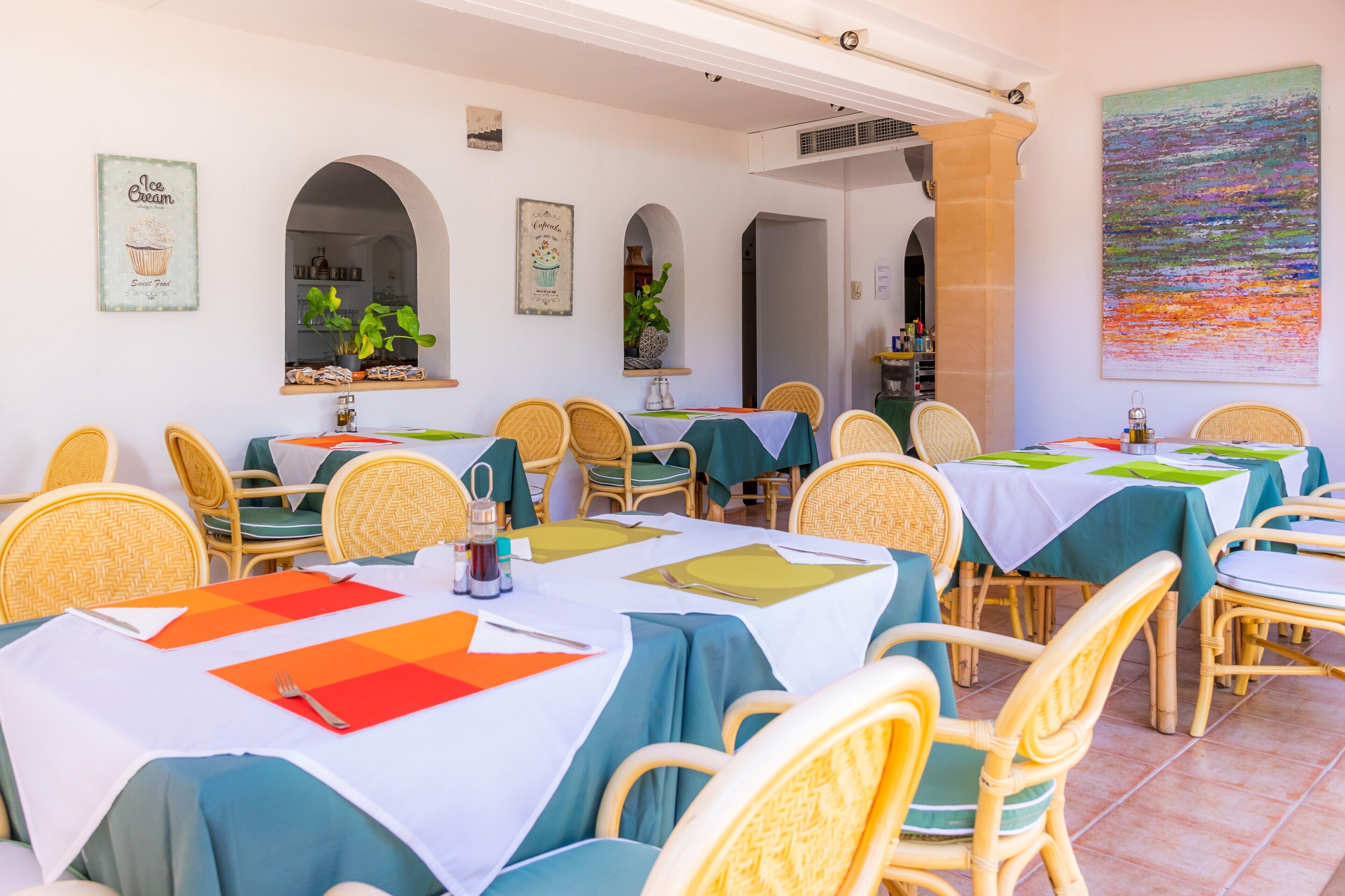 A dining area with multiple tables, wicker chairs, and green tablecloths.