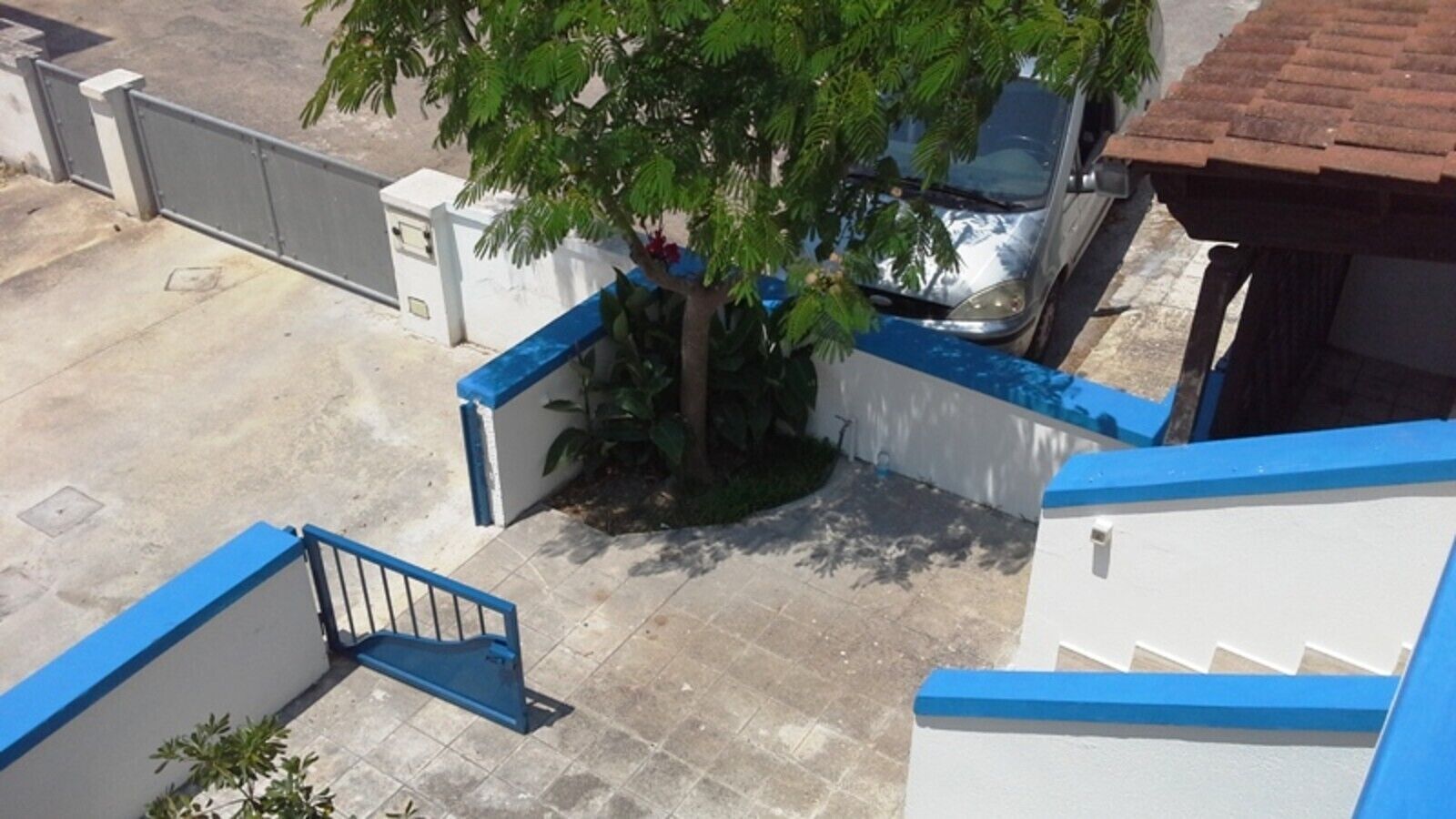 A gated parking area with a tree, a car, and a staircase leading to a building.