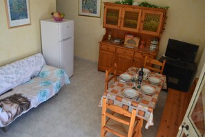 Un espace de vie compact comprenant un canapé, une table à manger pour quatre personnes, un réfrigérateur, des meubles de rangement en bois et un téléviseur.