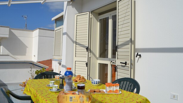 An outdoor dining area with a table set for two, a bottle of water, and a plate of food. - Central holiday home with terrace and garden; parking available (San Foca)