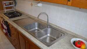 A kitchen with a double sink, stove, and a bowl of fruit. - Central holiday home with terrace and garden; parking available (San Foca)