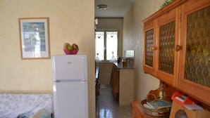 A compact kitchen with a refrigerator, a wooden cabinet, and a dining area with a table. - Central holiday home with terrace and garden; parking available (San Foca)