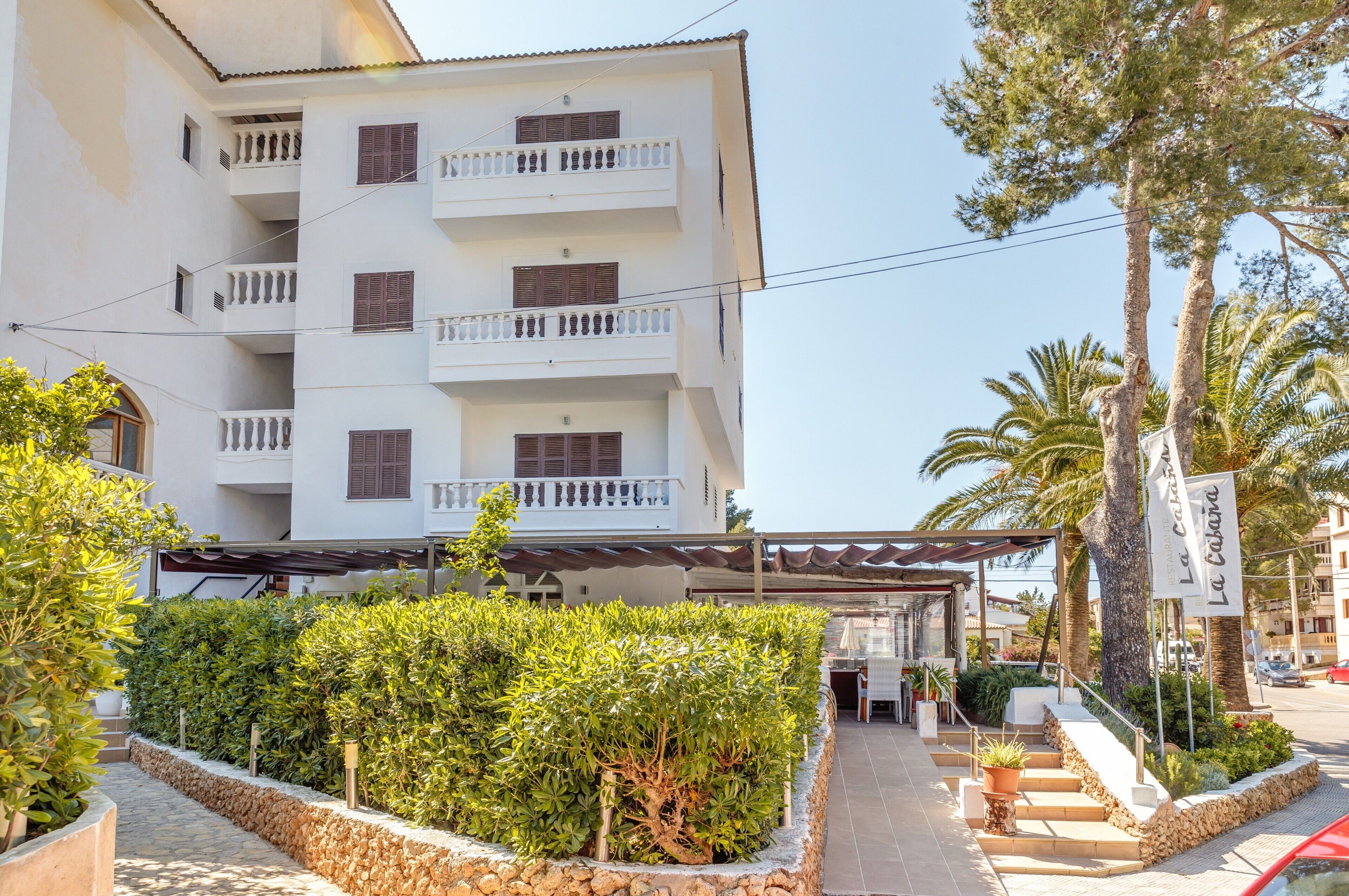 Un edificio de varios pisos con balcones, una zona de estar al aire libre techada y un jardín ajardinado con un camino de piedra.