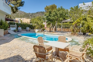 A pool area with wicker furniture, stone flooring, and surrounding greenery.
