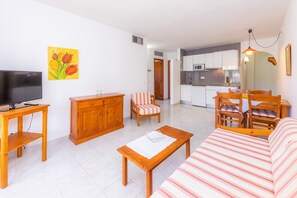 Uma sala de estar com televisão, móveis de madeira, um sofá e um espaço de refeições com cadeiras e uma mesa.
