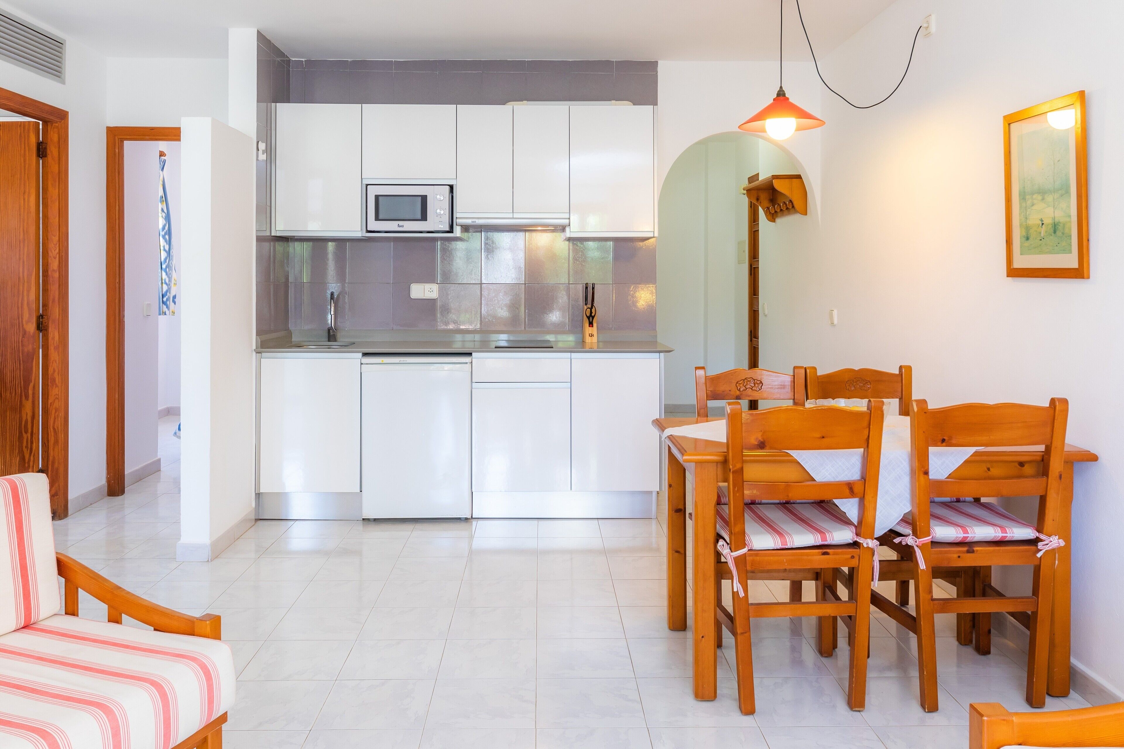A compact kitchen with white cabinets, a microwave, and a dining area with wooden chairs and a table.