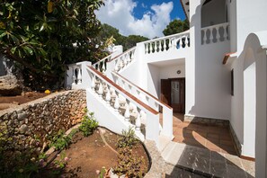A white building with a stone wall and a staircase leading to a door.