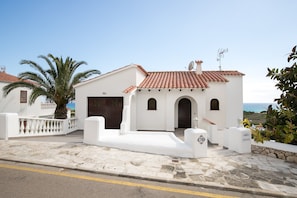 A white building with a tiled roof, a palm tree, and a clear view of the sea. - Vacation Home "Villa Belvedere 76" with Stunning Views and Pool (San Jaime)