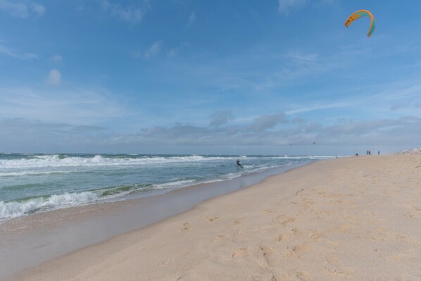 A beach with a sandy shore, ocean waves, and a person kite surfing.