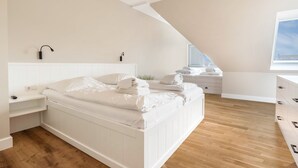 Un dormitorio moderno con cama blanca, suelo de madera, tragaluz, mesita de noche y mesilla.