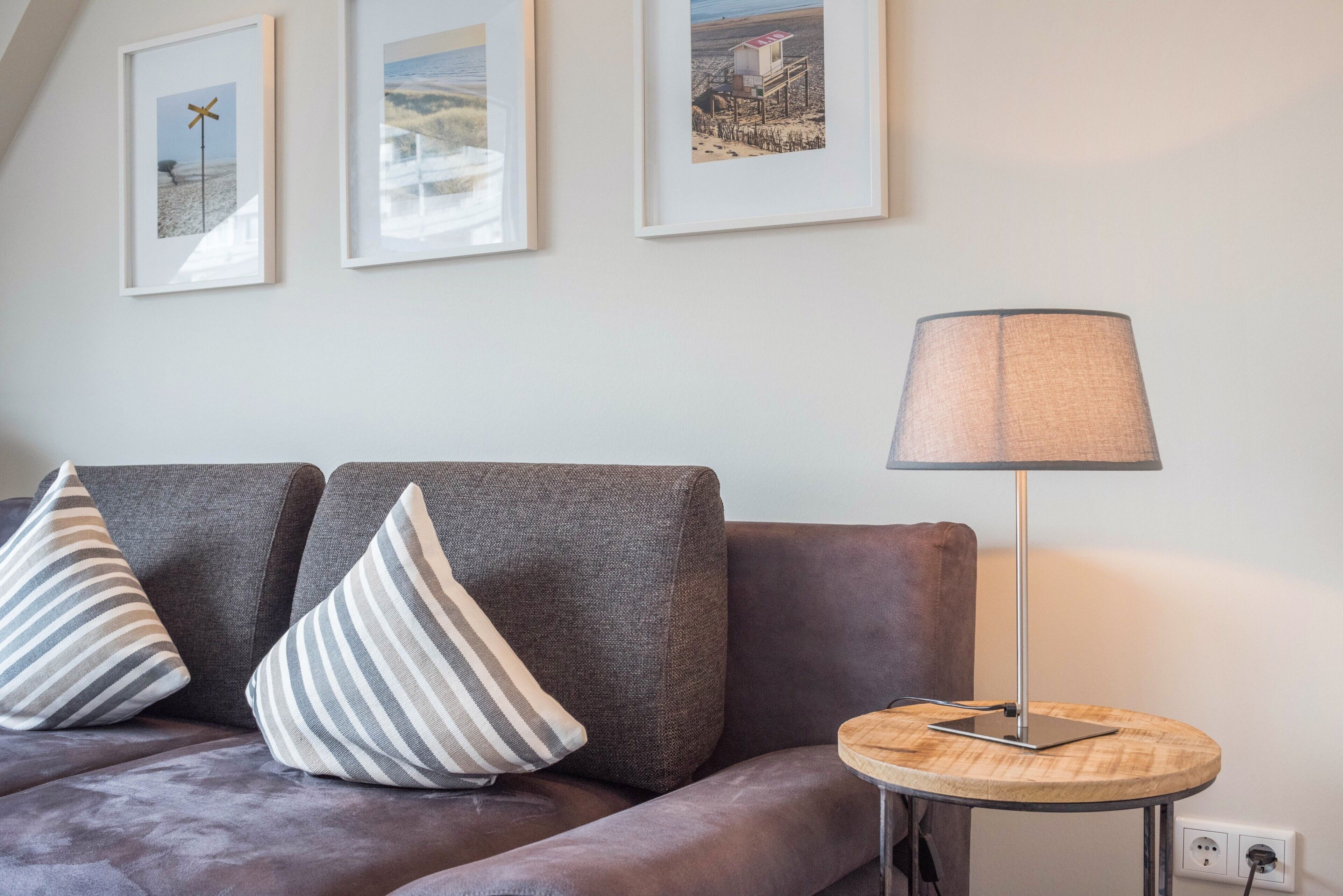 Un salon avec un canapé, deux coussins, une lampe et trois tableaux encadrés accrochés au mur.