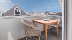 Un balcón con mesa de madera y sillas de mimbre, con vista a una zona residencial con casas y cielo despejado.