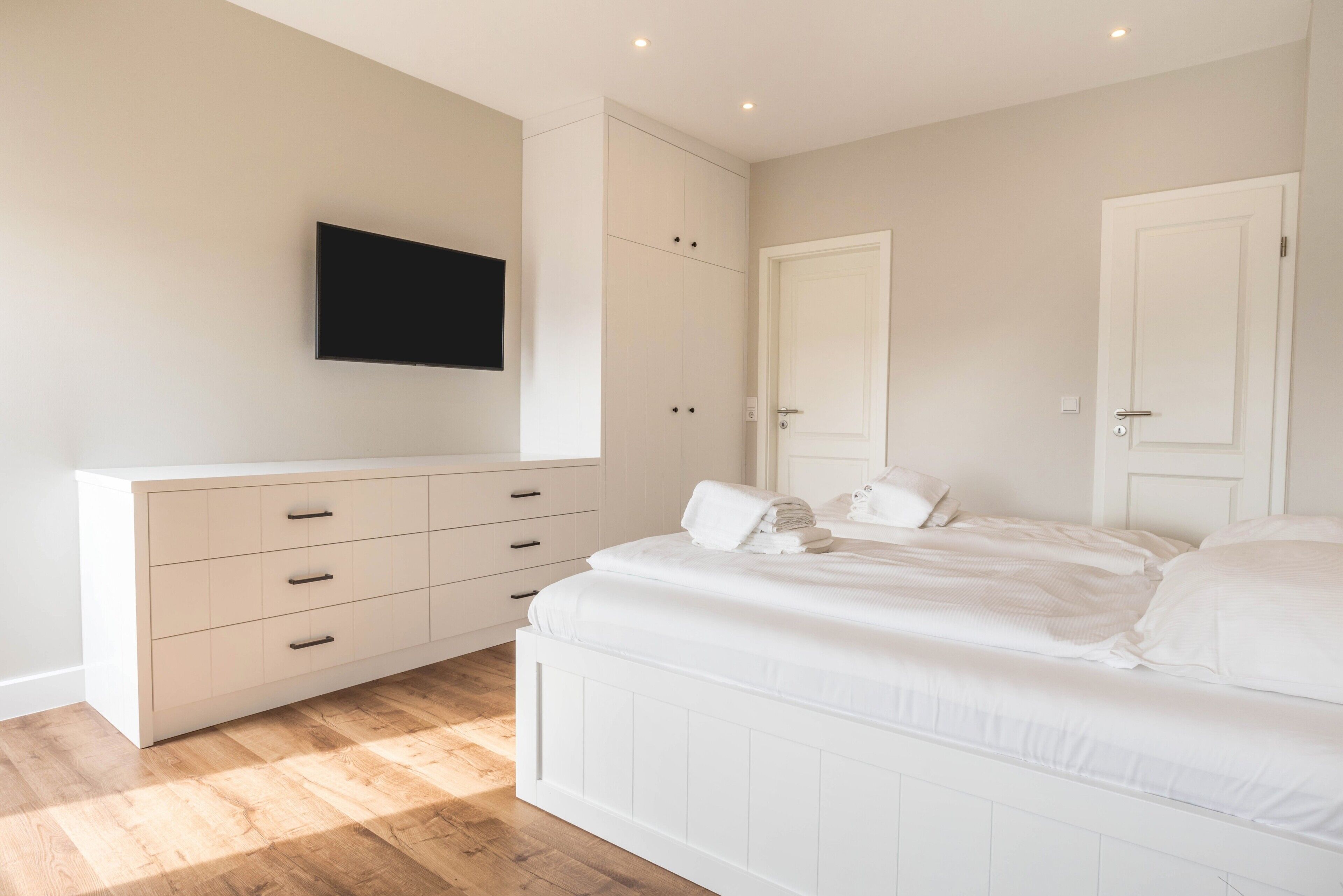A bedroom with a bed, a TV mounted on the wall, a wardrobe, and a door.