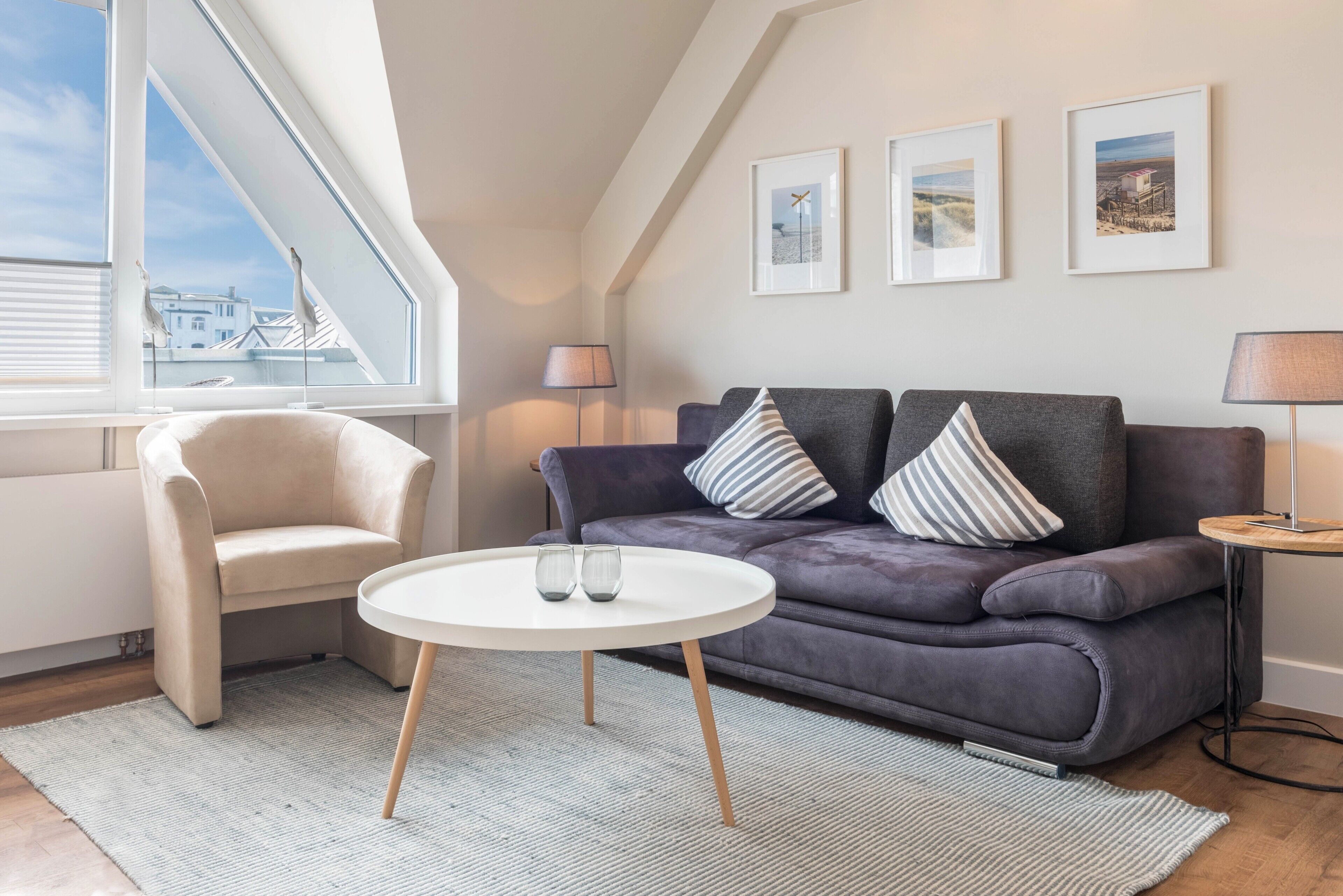 A modern living room with a sofa, armchair, round coffee table, and framed pictures on the wall.