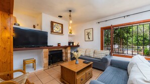 A living room with a TV, fireplace, sofa, and a view through a large window. - In the country with pool - Villa Can Garba (Felanitx)