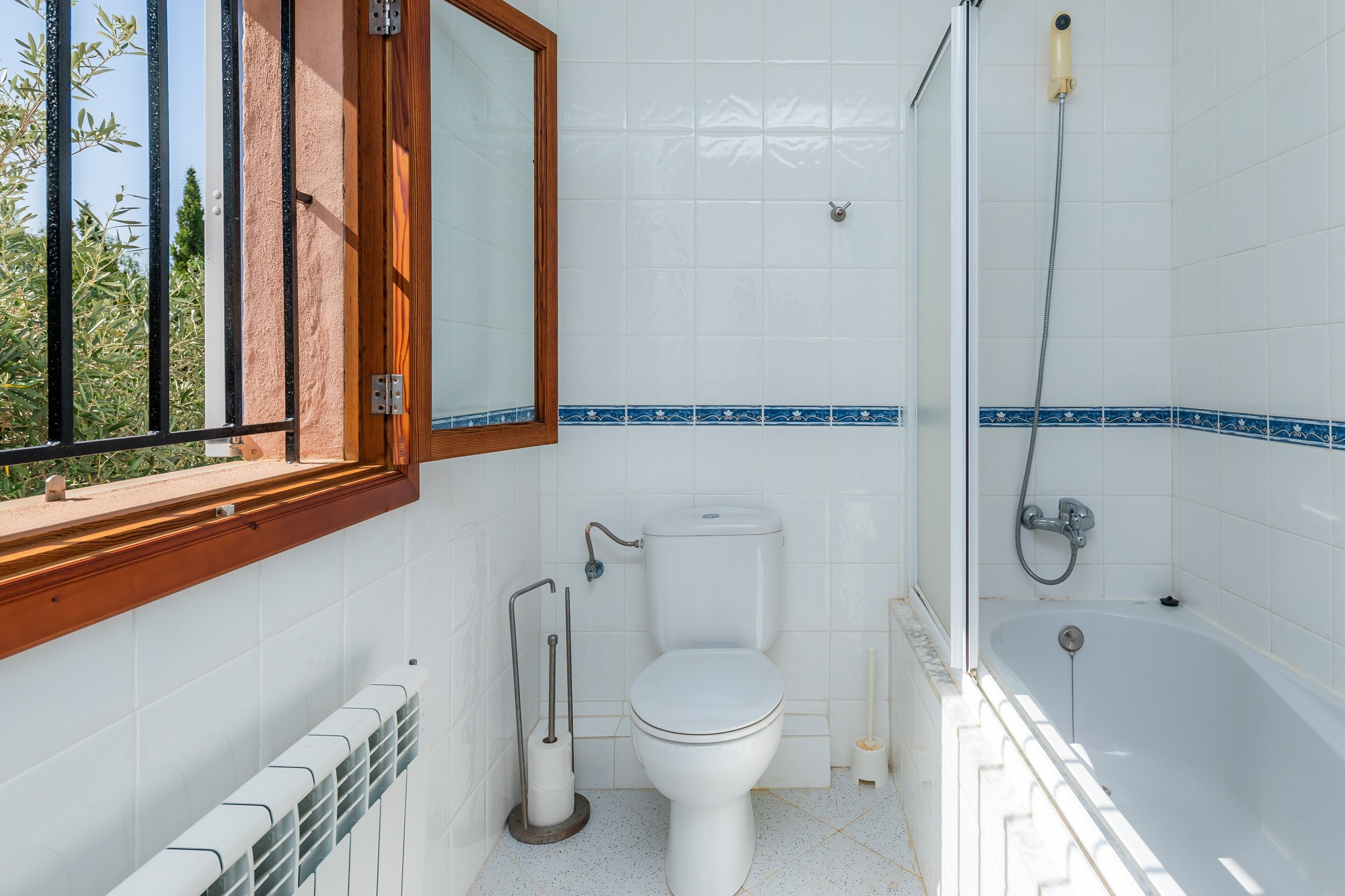A bathroom with a toilet, a bidet, a bathtub, and a window with a view of greenery.
