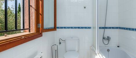 A bathroom with a toilet, a bidet, a bathtub, and a window with a view of greenery.