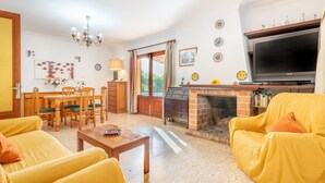 Ein Wohnzimmer mit gelber Möbel, einem Kamin, einem Fernseher und einem Essbereich.