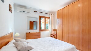Ein Schlafzimmer mit einem Bett, einem Holzschrank, einem Schminktisch, einem Spiegel, einem Fenster und einer Klimaanlage.