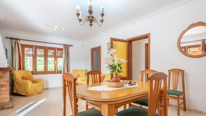 Ein Essbereich mit einem Holztisch, grünen Sitzgelegenheiten, einer Chandelüster und einem Fenster mit Vorhängen.