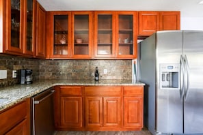 A kitchen with wooden cabinets, a granite countertop, a stainless steel refrigerator, and a coffee maker. - Eastside headquarters (Austin)