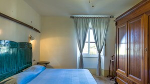 Un dormitorio con cama, un armario de madera, una mesita redonda y una ventana con cortinas.