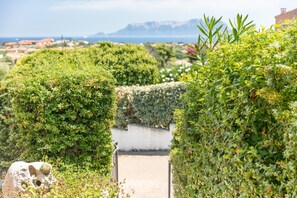 Un sentiero immerso nel verde conduce a un edificio bianco con vista sul mare e sulle montagne in lontananza.