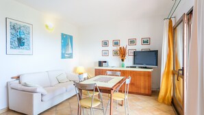 Ein Wohnzimmer mit einer Couch, einem Esstisch, Stühlen, einem Fernseher und gerahmten Bildern an der Wand.