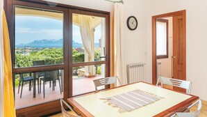 Ein Zimmer mit einer großen Schiebeglasdoor zum Außenbereich, einem Holztisch mit Stühlen, einer Uhr an der Wand und einer Heizung.