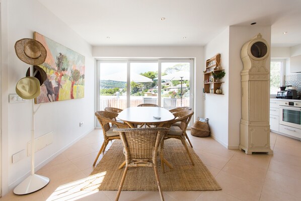 Un coin repas avec des chaises en osier, une table ronde et un grand tableau accroché au mur.