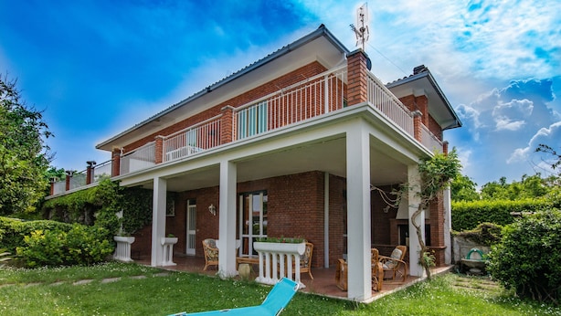 A two-story house with a covered patio, a lawn, and a blue lounge chair. - Lovely little house a few meters from the beach of the romantic Manerba (Manerba)