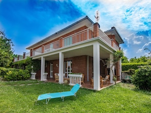 A two-story house with a covered patio, a lawn, and a blue lounge chair.