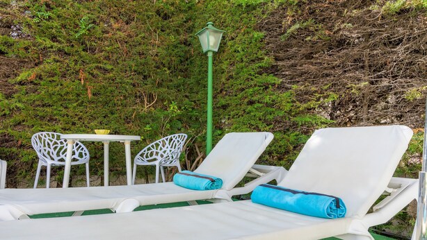 A set of white lounge chairs with blue towels, a green lamp post, and a table with chairs in a garden area.