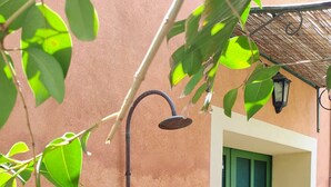 Un rociador de ducha adherido a una pared, una puerta verde y un banco de mimbre.