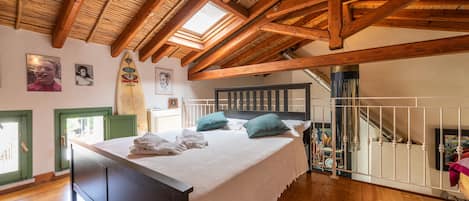 Un dormitorio con techo de madera, cama con ropa de cama blanca y vistas al exterior.