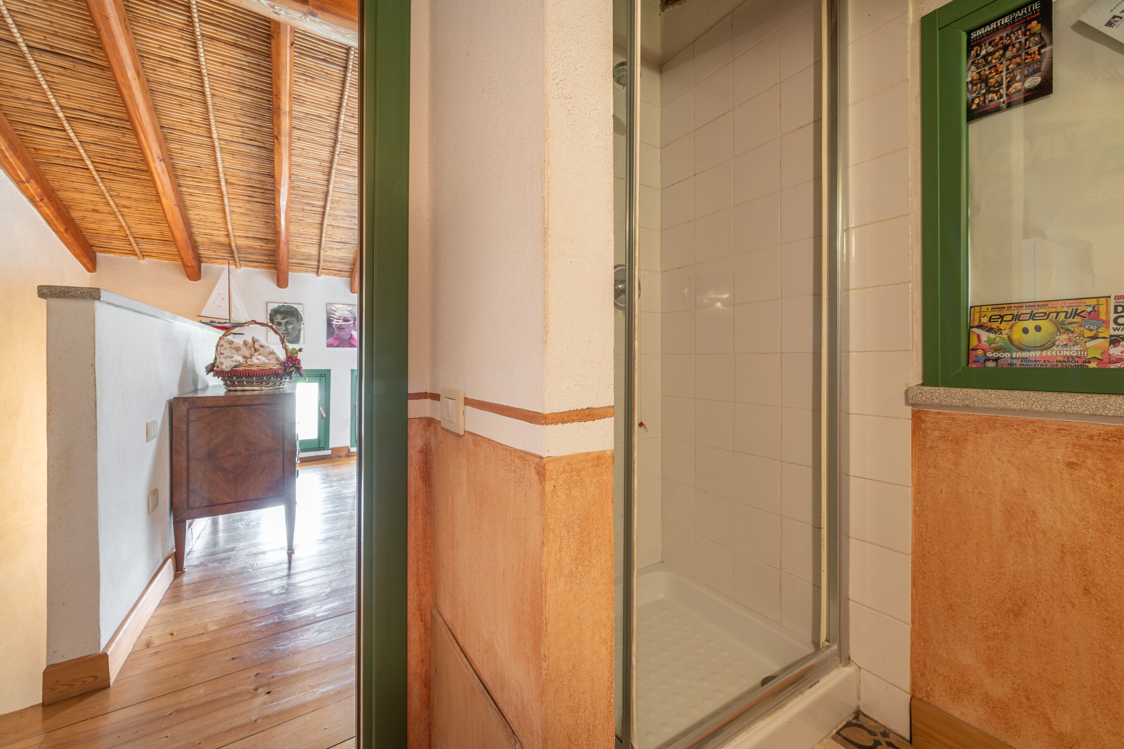A hallway with a wooden floor, a glass shower door, and a poster on the wall.