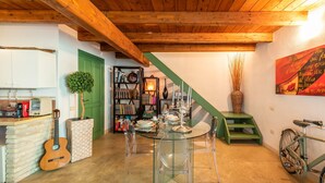 Un comedor con una mesa de vidrio, sillas, una guitarra, una estantería y una escalera verde.