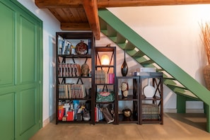 Un escalier avec des rampes vertes, un plafond en bois et une bibliothèque remplie de livres et d’objets décoratifs.