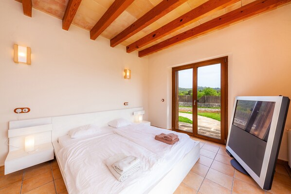 Ein Schlafzimmer mit einem Bett, Nachttischen, einem Fernseher und einer Schiebetür zum Außenbereich.