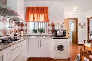 Une cuisine équipée d’un lave-linge, d’un four à micro-ondes et d’une fenêtre avec un rideau orange.