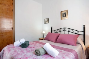 Un lit bien fait, avec une literie rose et blanche, une armoire en bois et une table de chevet avec une lampe.