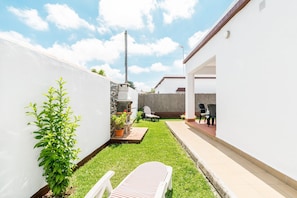 Un jardin avec une pelouse, un barbecue, une chaise blanche et une plante en pot.