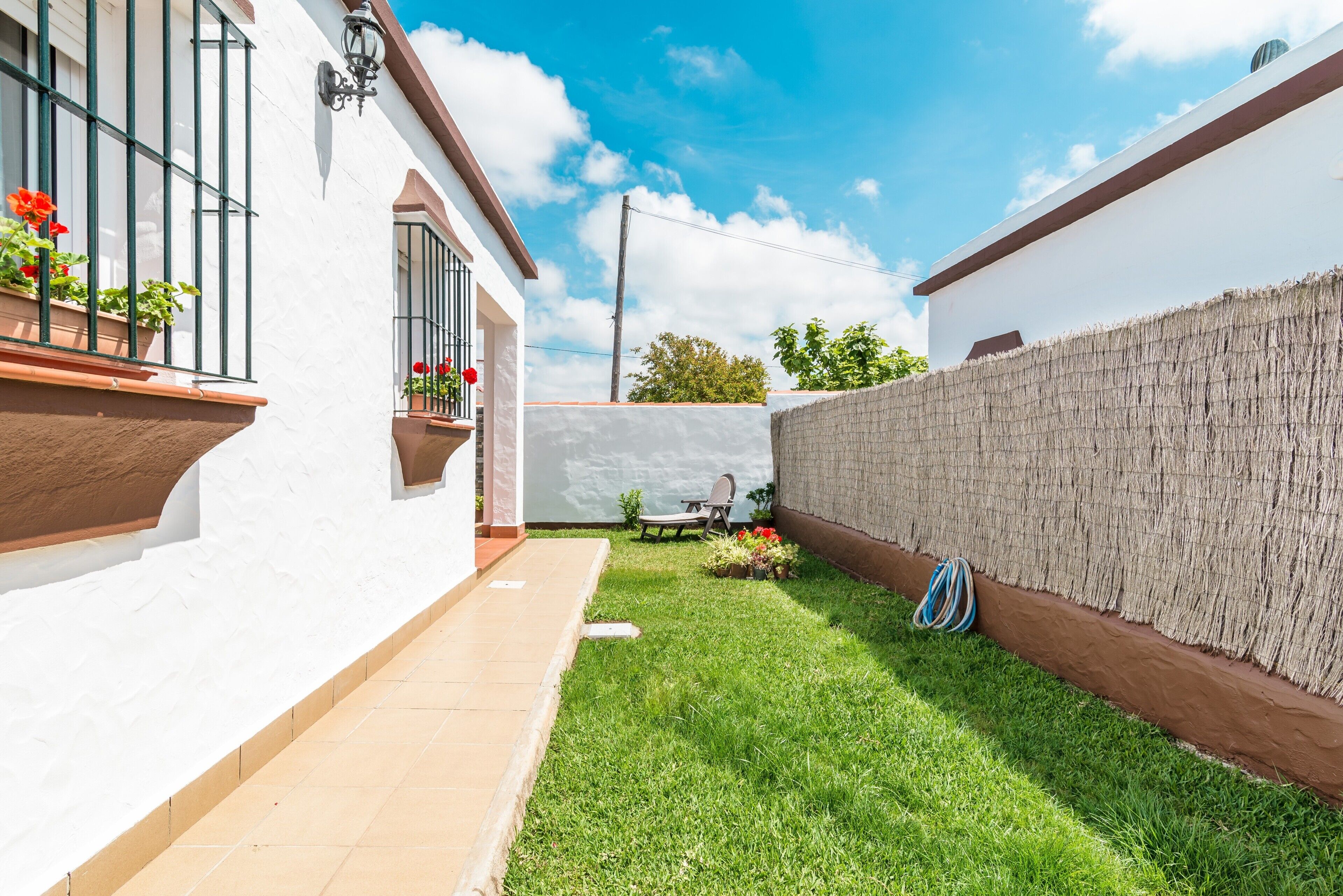 A white building with a tiled patio, a grassy area, and a wall with a woven texture.