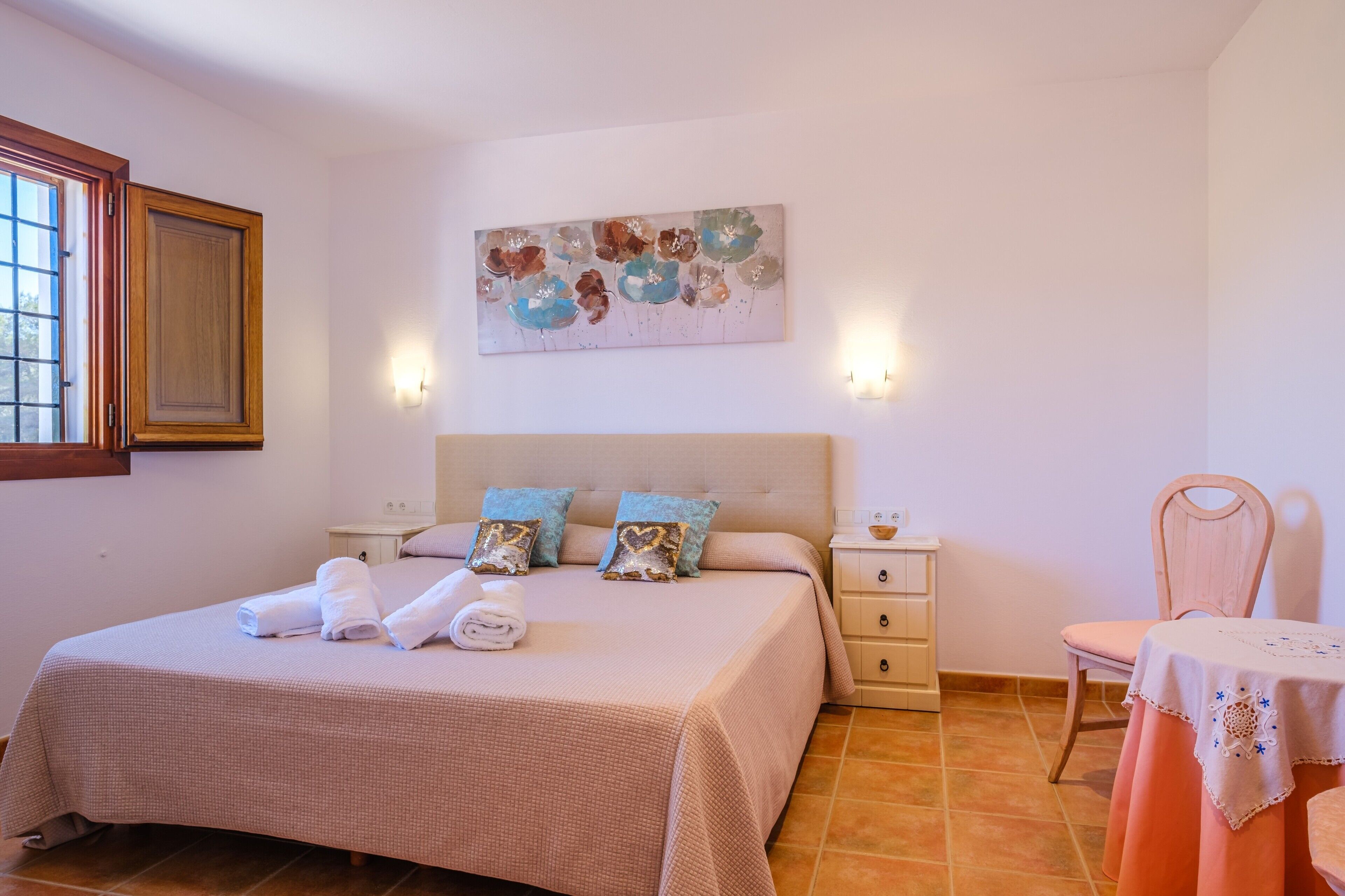 A bedroom with a bed, nightstands, a chair, a table, and a painting on the wall.