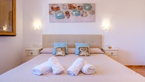Een netjes opgemaakt bed met twee kussens, een nachtkastje met een schaal en een aan de muur hangend kunstwerk.